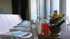 A row of white chairs with towels, a bottle of red liquid, and a vase with yellow flowers on a textured surface. - Steigenberger Hotel Stadt Hamburg (Wismar)