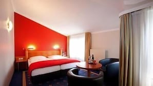 A hotel room with a bed, a desk, a chair, a lamp, and a window with curtains. - Steigenberger Hotel Stadt Hamburg (Wismar)
