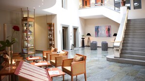A spacious lobby with a high ceiling, a staircase, and seating areas. - Steigenberger Hotel Stadt Hamburg (Wismar)