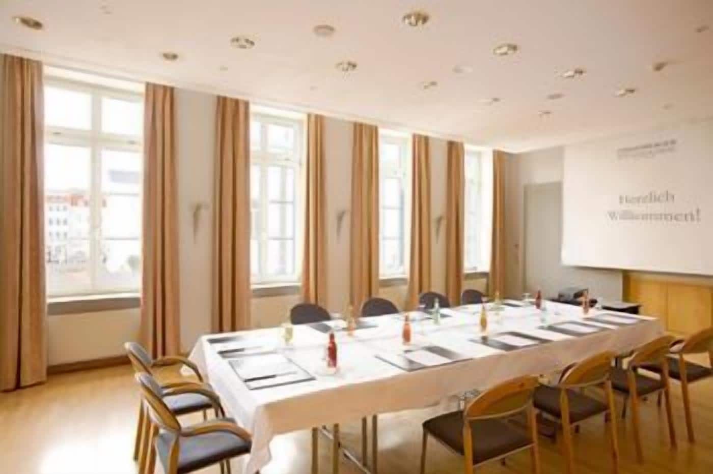 Ein Konferenzraum mit einem langen Tisch, Stühlen und einer Präsentationsleinwand.