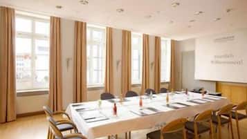 Ein Konferenzraum mit einem langen Tisch, Stühlen und einer Präsentationsleinwand.