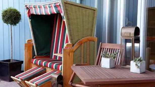A wicker chair with a striped cushion, a wooden table with a potted plant, and a mailbox. - Steigenberger Hotel Stadt Hamburg (Wismar)
