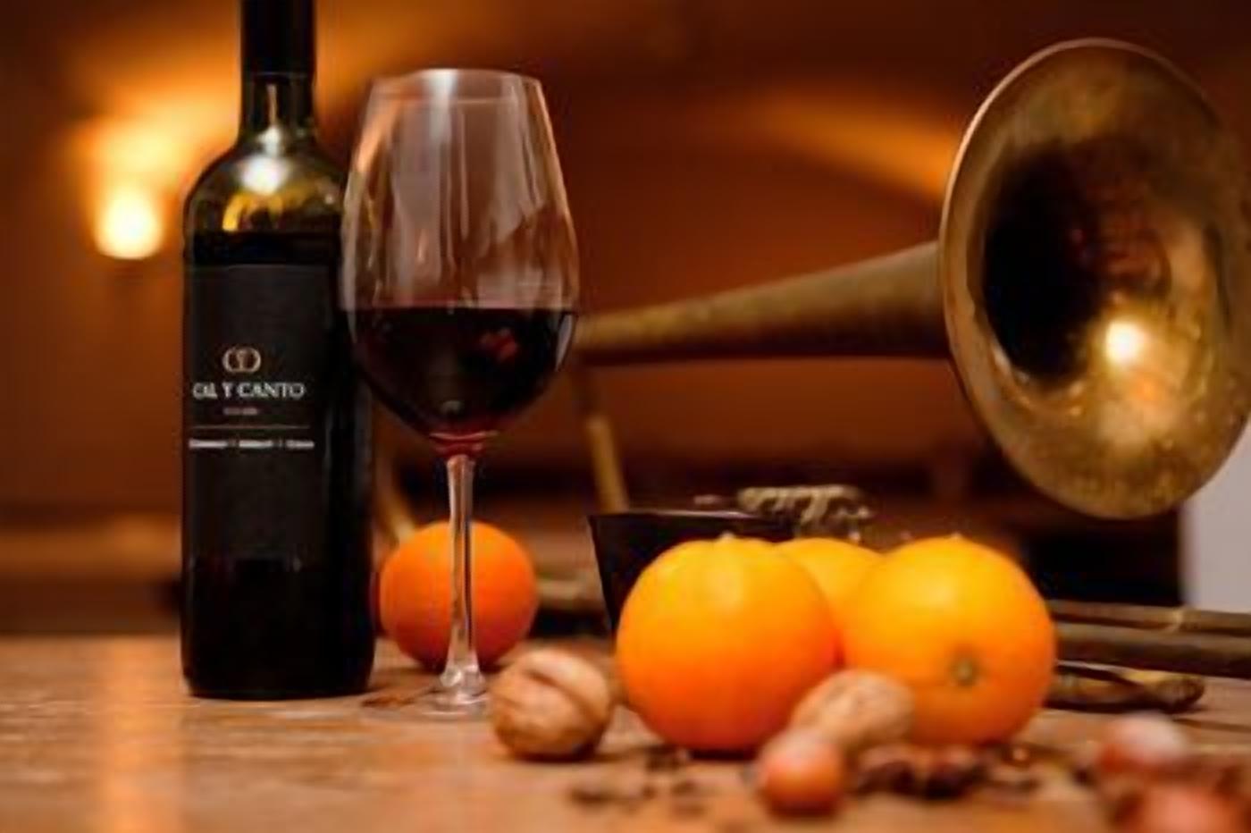 A bottle of wine, a glass, and oranges on a table.