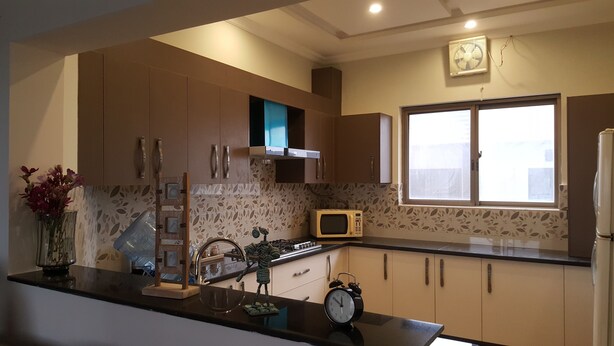 A modern kitchen with a microwave, stove, and clock on the counter. - Valley View Villa (Rawalpindi)