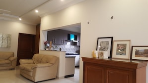 A living room with a beige armchair, a wooden cabinet, and a kitchen area in the background. - Valley View Villa (Rawalpindi)