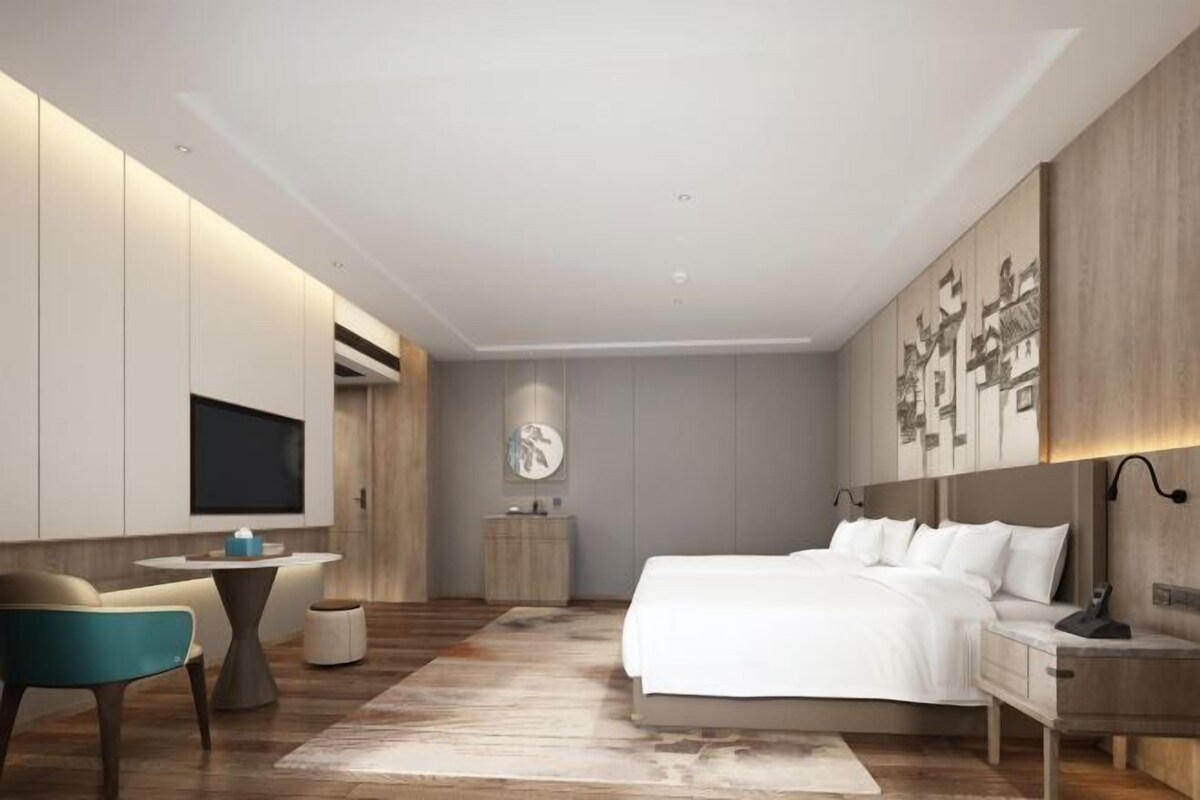 Un dormitorio moderno con una cama grande, mesitas de noche, un escritorio y un televisor montado en la pared.