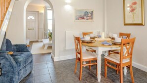 Un coin repas avec une table en bois dressée pour quatre personnes, entourée de chaises assorties. Un arc donne accès à un couloir où se trouve une porte blanche.