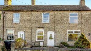 Une maison en pierre au design traditionnel, dotée d’une porte centrale, de deux fenêtres à l’étage supérieur et d’un petit jardin agrémenté de murs en pierre et de plantes.