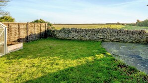 Un mur de pierres et une clôture en bois se dressent dans une zone herbeuse, sous un ciel dégagé.