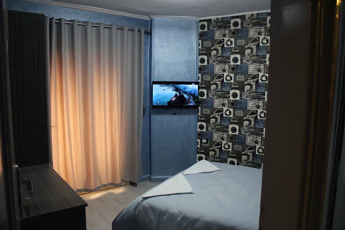 Ein Hotelzimmer mit einem Bett, einem an der Wand befestigten Fernseher und einem Vorhang.