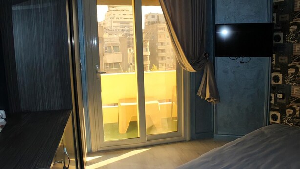 A hotel room with a sliding glass door to an outdoor balcony, a bed, and a flat-screen TV mounted on the wall. - Sunset Hotel Cairo - Hostel (Cairo)