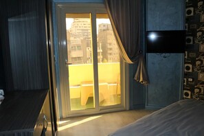 A hotel room with a sliding glass door to an outdoor balcony, a bed, and a flat-screen TV mounted on the wall. - Sunset Hotel Cairo - Hostel (Cairo)