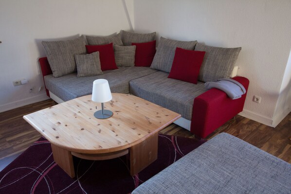 A modern living room with a grey sofa, red cushions, a wooden coffee table, and a grey armchair.