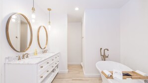 A modern bathroom with a white vanity, two large mirrors, a bathtub, and a shower. - Benson Guest House (Uvalde)