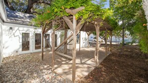 A wooden pergola with climbing plants, a gravel pathway, and a white building with doors and windows. - Benson Guest House (Uvalde)