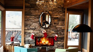 A cozy living room with a stone fireplace, a chandelier, and a large mirror above it. - Chalet lovers in Switzerland (Saint George)
