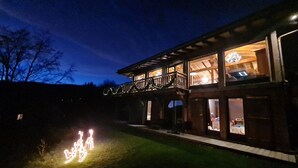 A two-story wooden house with a balcony, a covered porch, and a well-lit interior. - Chalet lovers in Switzerland (Saint George)