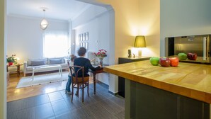 Uma cozinha moderna com bancada de madeira, geladeira e área de refeições com mesa e cadeiras brancas.