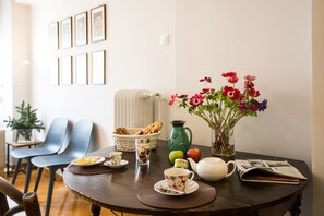 A dining table with a basket of bread, a pitcher, a vase of flowers, plates with food, and a teapot.