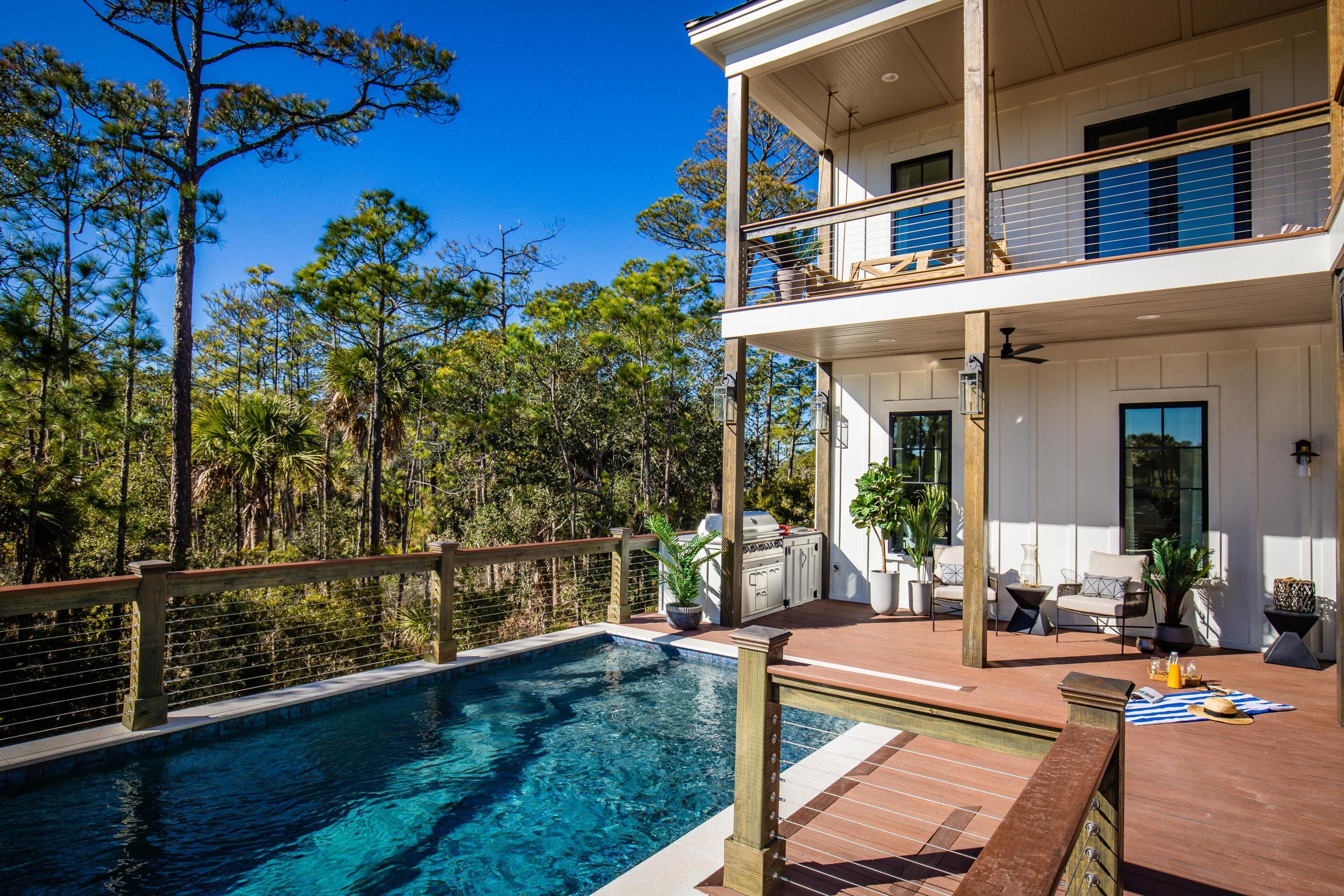 A two-story house with a swimming pool, outdoor furniture, and a wooden deck.