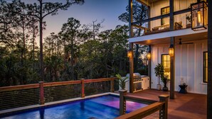 Ein zweistöckiges Haus mit Pool, Sitzgelegenheit im Freien und einem Balkon mit Blick auf eine bewaldete Landschaft.