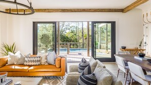 Ein modernes Wohnzimmer mit großem Fenster, Holzboden und Blick auf einen Außenpool.