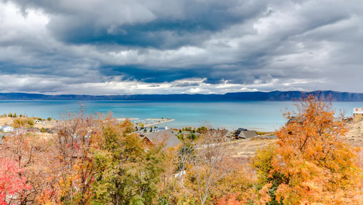 A coastal town with houses near a body of water, surrounded by autumn-colored trees.