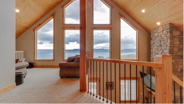 Un espacioso dormitorio tipo loft con amplias ventanas, una chimenea de piedra y una zona de estar acogedora.