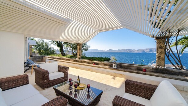 A sunlit outdoor seating area with wicker furniture and a glass table, overlooking a scenic coastal view. - CAN RAMIS -  Seafront house with panoramic views. (Cielo de Bonaire)