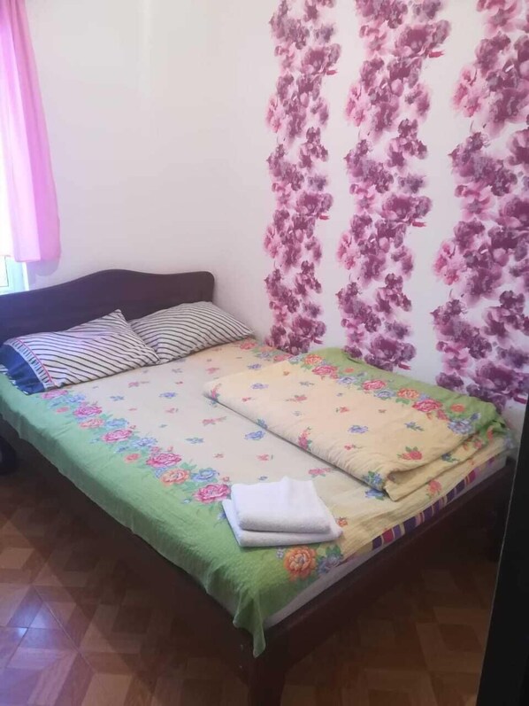 Un dormitorio con cama, almohadas, colcha verde y papel tapiz floral.