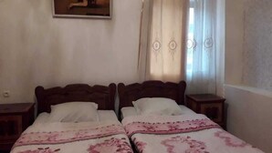 Un dormitori amb dos llits de fusta, una tauleta de nit a cada costat, un quadre a la paret i una finestra amb cortines.