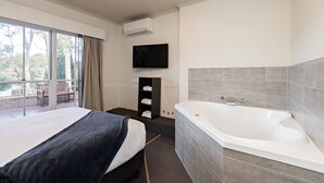 Un dormitorio moderno con una cama grande, una bañera integrada y un televisor en la pared.
