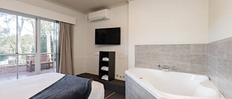 Un dormitorio moderno con una cama grande, una bañera integrada y un televisor en la pared.