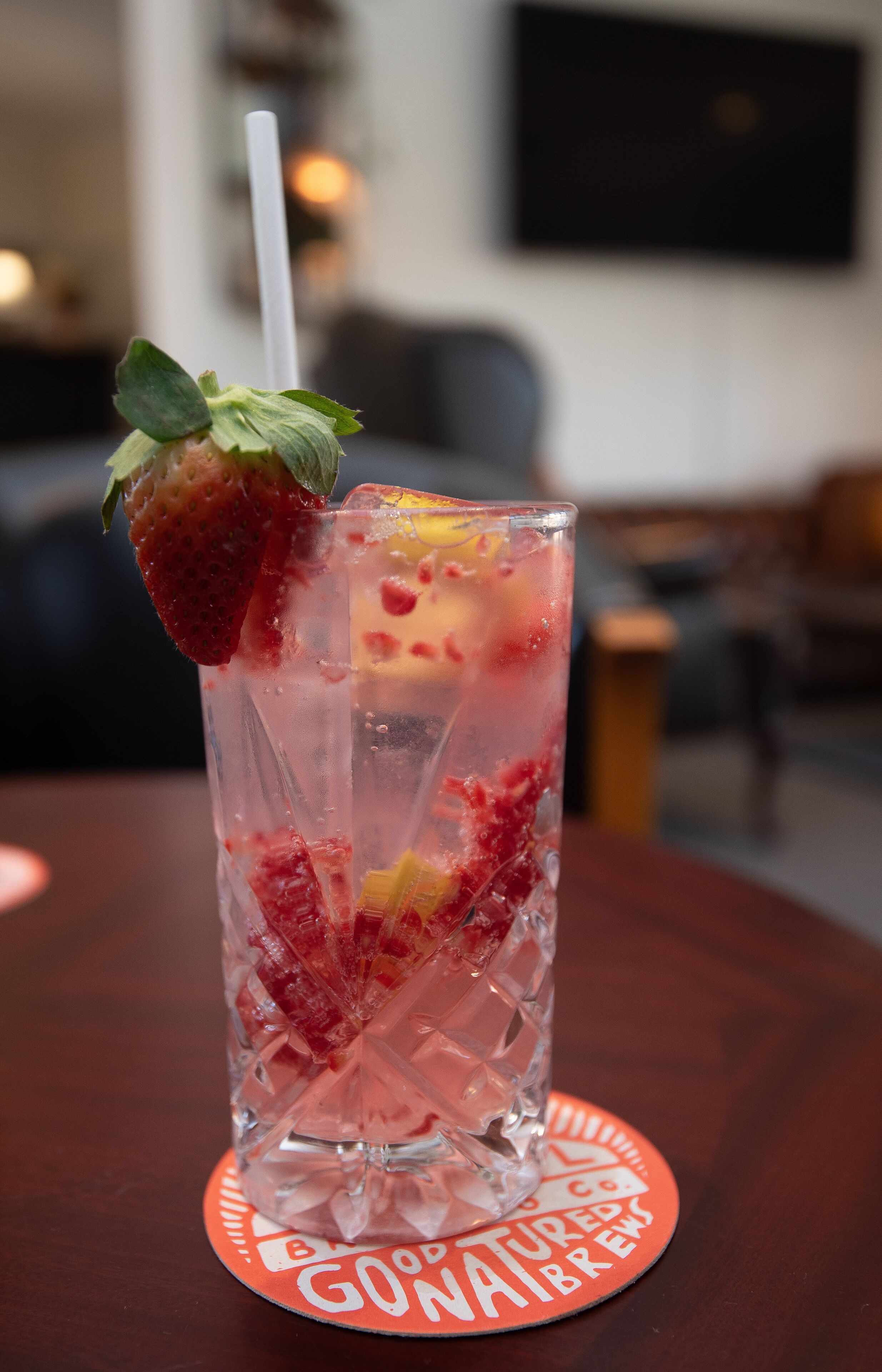 A tall glass with a strawberry and a straw on a coaster with text.