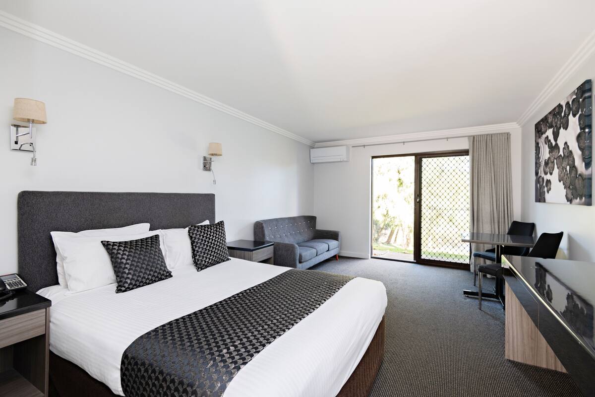 Una habitación de hotel con una cama grande, un sofá, un escritorio y vistas al exterior.