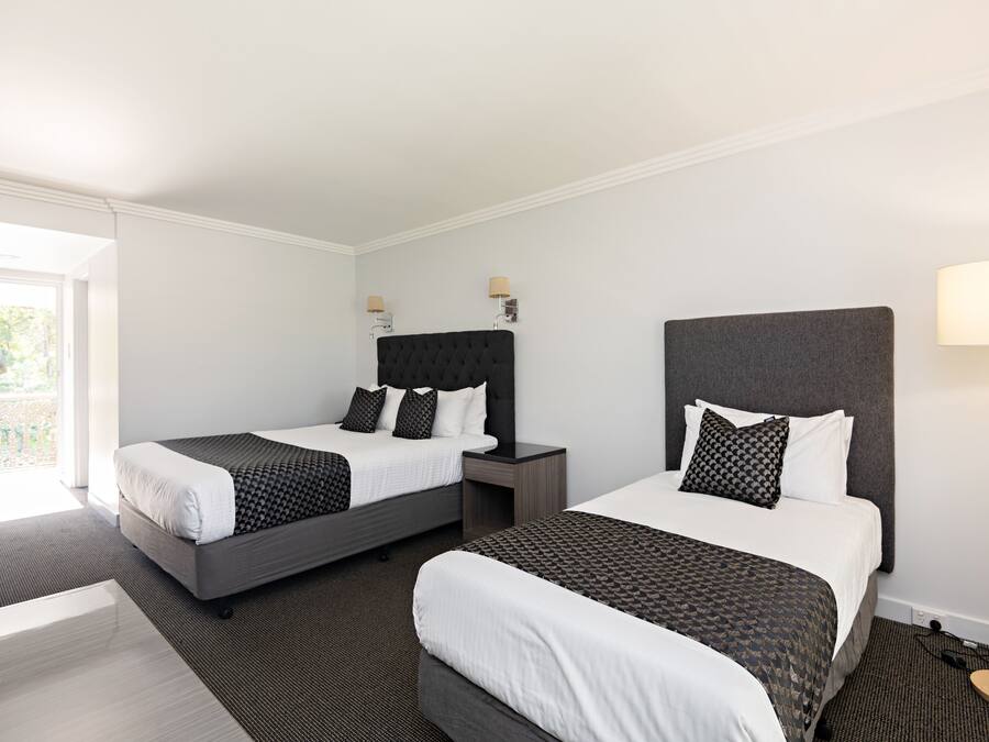 A hotel room with two beds, a bedside table, a lamp, and a view of the outdoors.