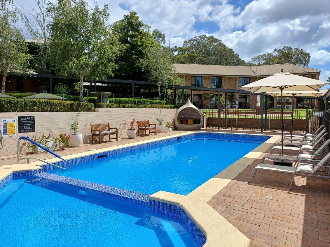 A swimming pool with a tiled edge, lounge chairs, and a covered seating area.