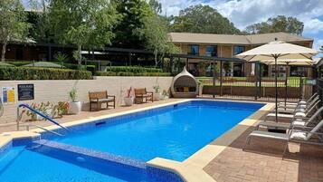 A swimming pool with a tiled edge, lounge chairs, and a covered seating area.