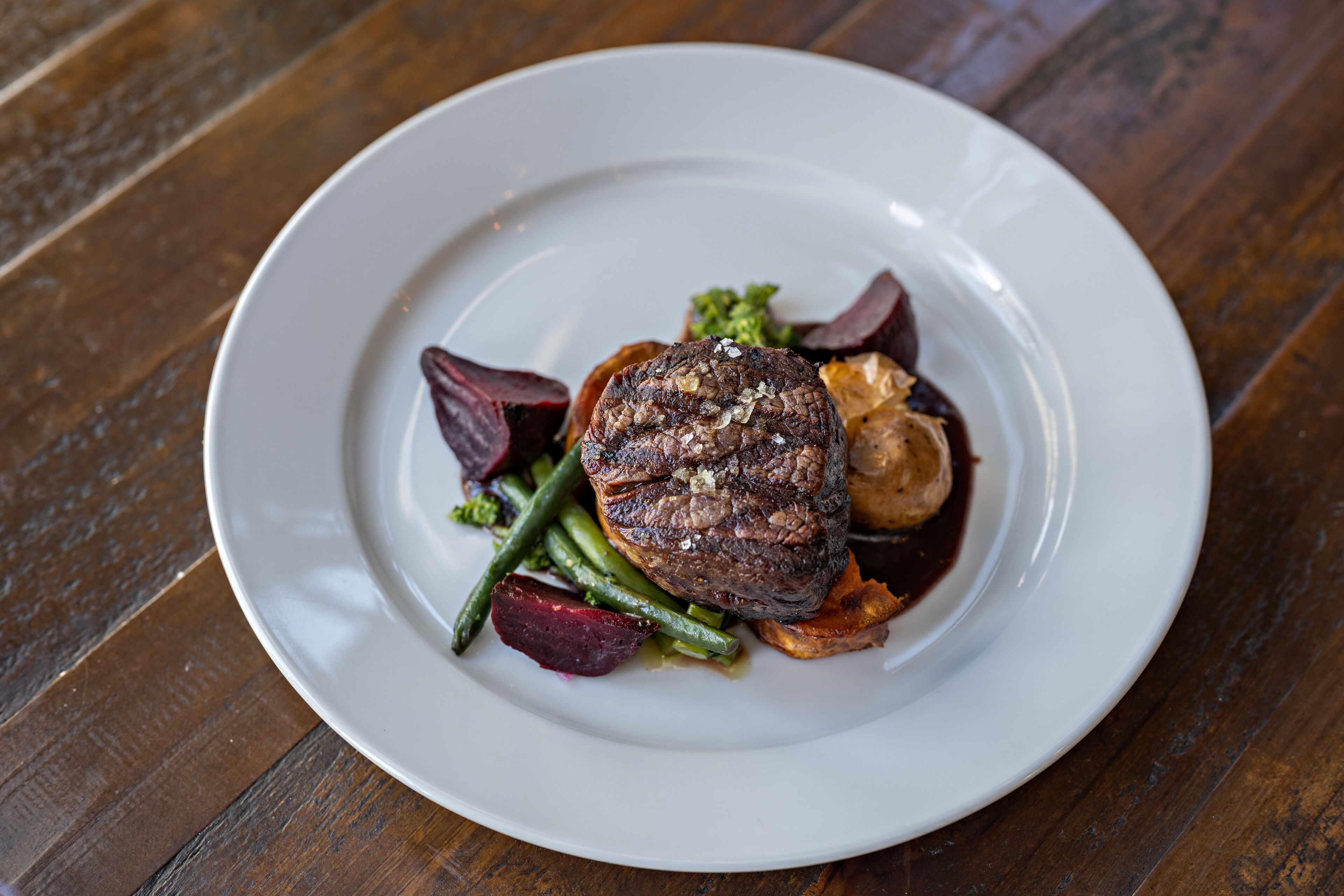 A plate of food with a steak, green beans, and red vegetables on a white plate.