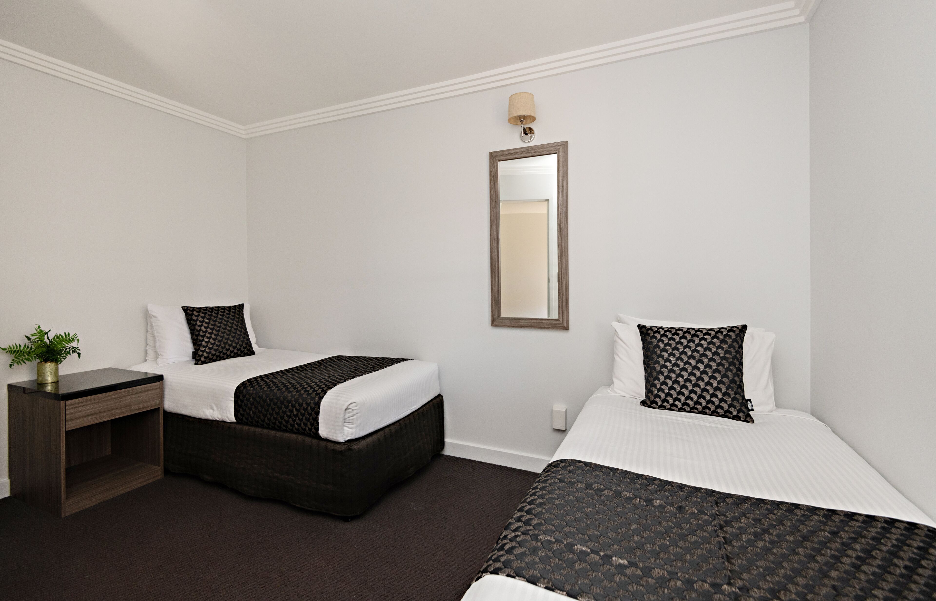A hotel room with two beds, a nightstand, a lamp, and a mirror.