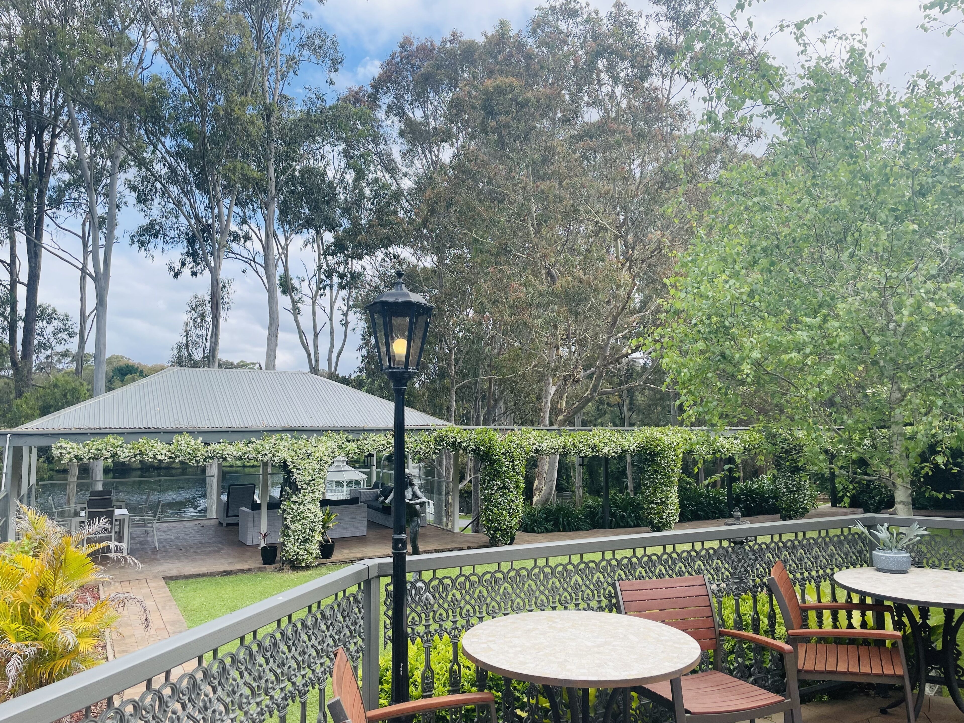 An outdoor patio with a covered seating area, a decorative lamp, and a view of trees.