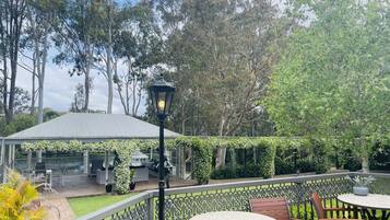An outdoor patio with a covered seating area, a decorative lamp, and a view of trees.