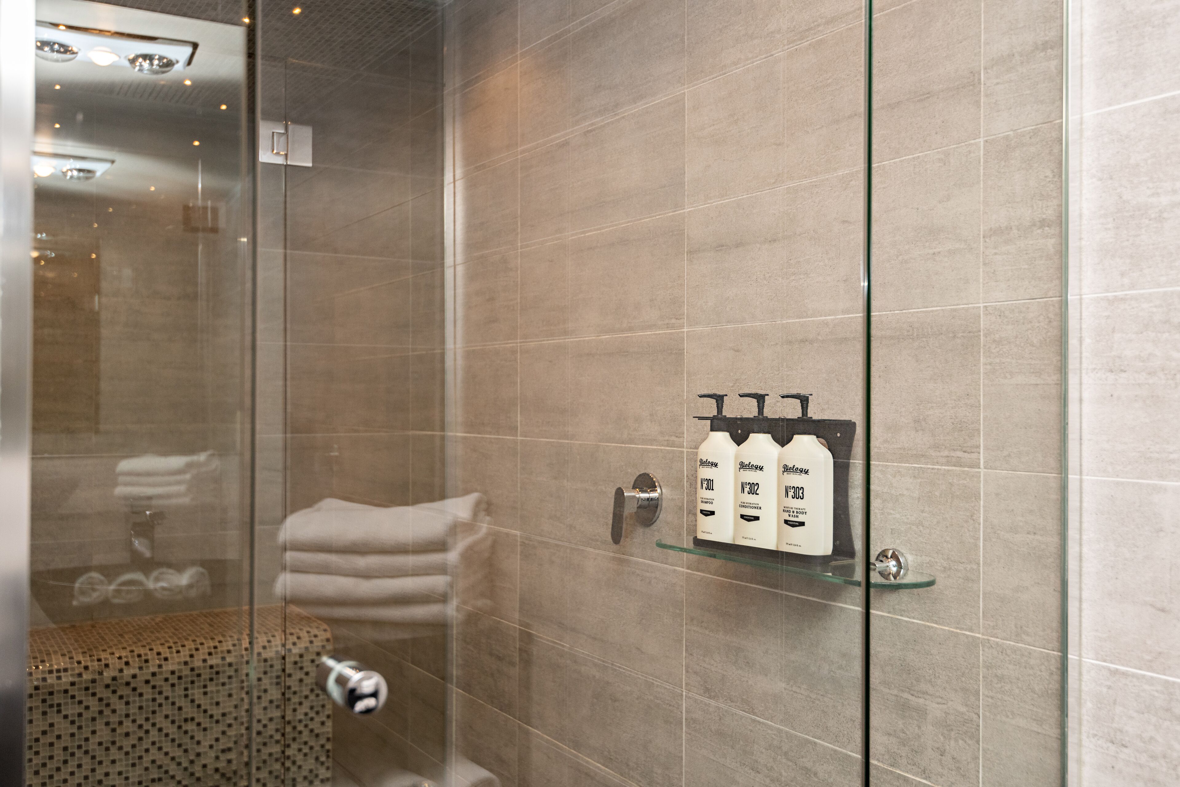Un baño moderno con cabina de ducha de vidrio, repisa de vidrio con artículos de aseo y suelo estampado.