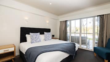 Habitación de hotel moderna con una cama grande, una mesita de noche, una silla y vistas al exterior a través de amplios ventanales.