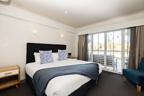 Een moderne hotelkamer met een groot bed, een nachtkastje, een stoel en uitzicht op de omgeving door grote ramen.