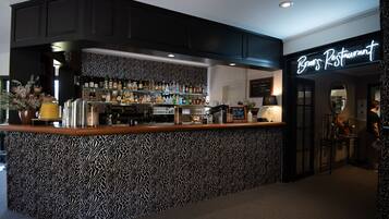 Zona de bar con mostrador estampado de cebra, estantes con botellas y un letrero de neón que dice 'Brow's Restaurant'.