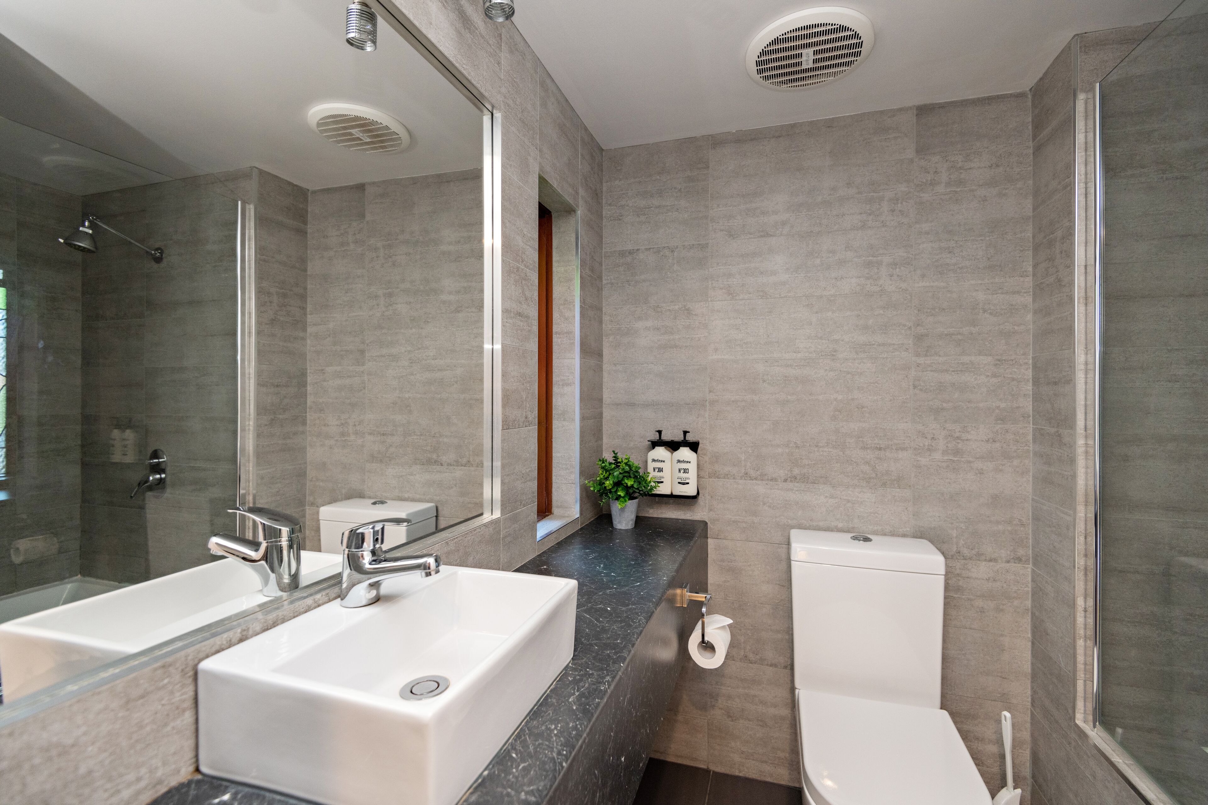 A modern bathroom with a large mirror, a white sink, a toilet, and a shower area.