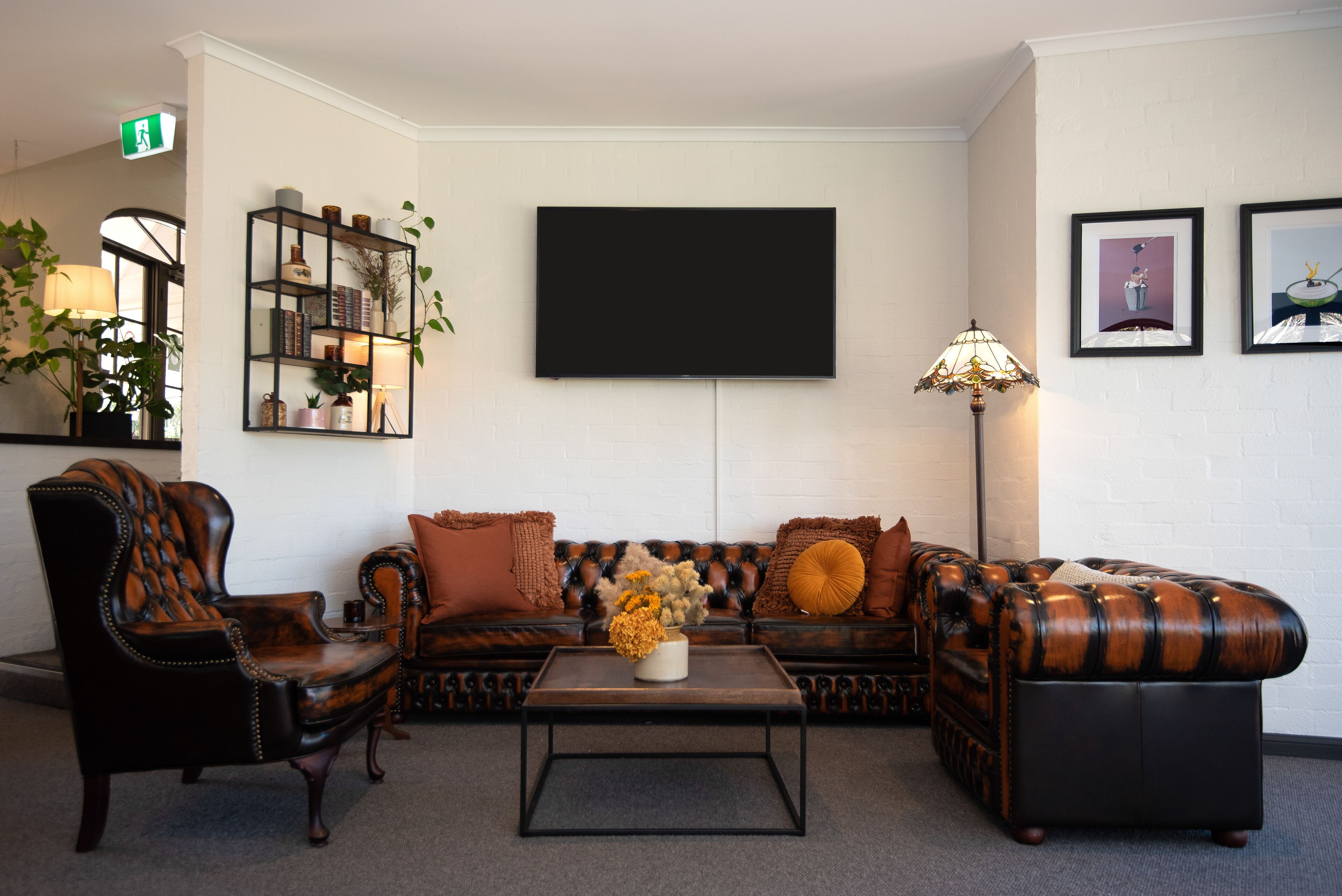 A living room with a sofa, armchairs, a coffee table, a TV, a bookshelf, and a lamp.