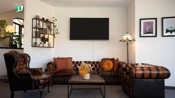 Un salon comprenant un canapé, des fauteuils, une table basse, un téléviseur, une bibliothèque et une lampe.