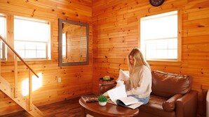 A wooden cabin interior with a staircase, a brown leather sofa, a wooden coffee table, and a mirror on the wall. - White Mountains Lakeside Log Cabin Solo Retreat (Bethlehem)